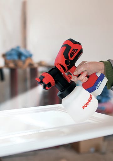 Sun Joe 24-volt cordless handheld paint sprayer being used to paint a surface white.